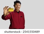 Asian man wearing red shirt cheerful showing plastic credit card and smiling, camera shot at credit card