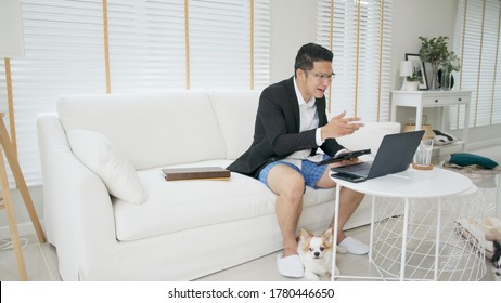 Asian man wearing a suit or business wear on top and sweatpants or boxers on bottom. Businessman video conference using laptop and tablet online meeting.Working from home and Working remotely.