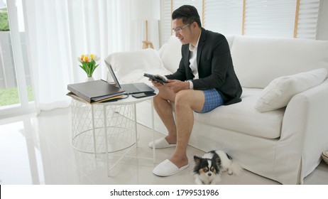 Asian Man Wearing A Suit Or Business Wear On Top And Sweatpants Or Boxers On Bottom. Businessman Video Conference Using Laptop And Tablet Online Meeting.Working From Home And Working Remotely.