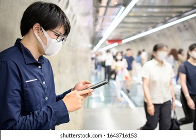 Asian man wearing surgical face mask using smartphone in subway tunnel with crowded people walking. Wuhan coronavirus (COVID-19) outbreak prevention in public area. Health care and medical concept - Powered by Shutterstock