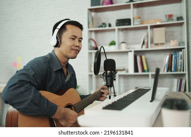Asian Man Wearing White Headphones Play Guitar And Sing A Song And Learning Online With Mobile Phone And Compose Writing Song Or Record Sound With A Microphone And Use Computer Recording Music Program