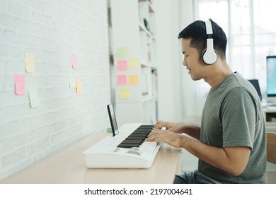 Asian Man Wearing White Headphones Play Piano And Sing A Song And Learning Online With Mobile Phone And Compose Writing Song Or Record Sound With A Microphone And Use Computer Recording Music Program