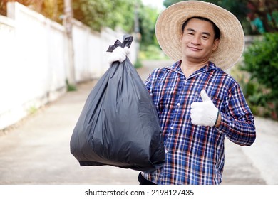 Asian Man Wears Hat, Plaid Shirt, And Gloves, Holds Black  Plastic Bag That Contains Garbage Inside, Thumbs Up. Concept : Garbage Keeper. Waste Management. Environment Solving. Cleaning Public Place. 