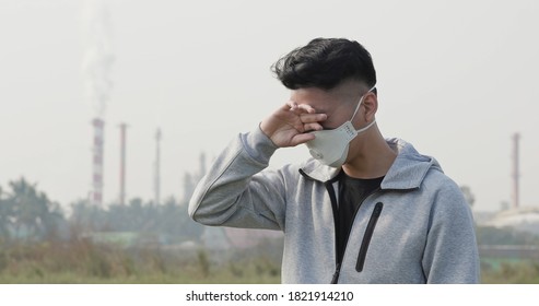 Asian Man Wears Protective N95 Mask And Has Itchy Eyes Because Air Pollution In Front Of Factory