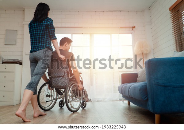 An Asian man in a wheelchair in the home after a\
car accident and his wife to give encouragement. The concept of\
Mutual care and new technology has made people with disabilities\
Equality in society.