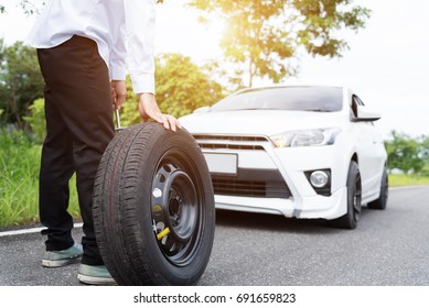 Asian Man With A White Car That Broke Down On The Road.Changing Tire On Broken Car On Road.