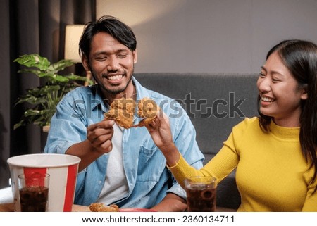 Asian man and woman couple eating fried chicken happily inside their home celebrating the weekend.