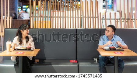 Asian man and woman eating food on table by one person one table for social Distancing 6 feets concept protection of Coronavirus Covid-19 at food court in Bangkok, Thailand.