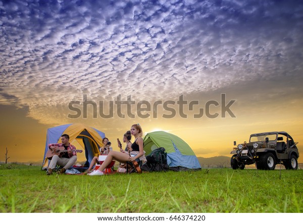 asian man and woman\
enjoy party camping, play guitar and singing song at rim of lake\
with sunset in background