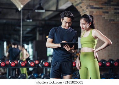 Asian man and woman exercise training in fitness gym. Young male trainer using tablet for schedule exercise training to fitness female. Workout training in fitness gym. - Powered by Shutterstock