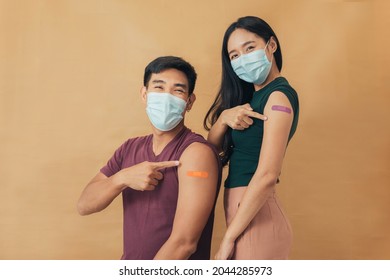 Asian Man And Woman Showing Shoulders After Getting A Vaccine. Happy Couple Showing Arm With Band-aids On After Vaccine Injection.