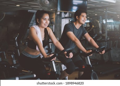 Asian Man And Woman They Are Enjoys Cycling In The Gym Because It Keeps His Legs Strong And Healthy.