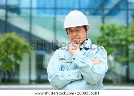 An Asian man in work clothes looking troubled.