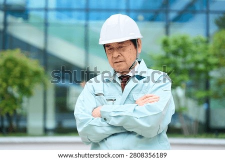 An Asian man in work clothes looking troubled.