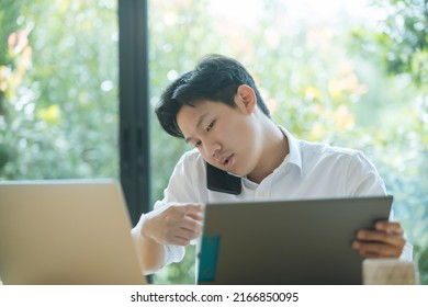 Asian Man Working Busy While Making Phone Call And Using Laptop At Home