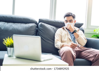 Asian Man Working From Home Wearing Protective Facemask Sitting On Sofa In Living Room Feeling Sick In Video Call With Workers Using Laptop, Quarantine Self Isolation, Coronavirus Covid-19 Pandemic