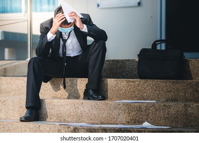 Asian Man Working In A Masked Office Sitting Sad And Stressed From Being Unemployed And Fired From The Company. Unemployment Concept Fails During Covid Strain Omicron, Delta