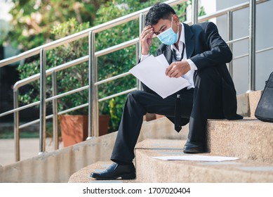 Asian Man Working In A Masked Office Sitting Sad And Stressed From Being Unemployed And Fired From The Company. Unemployment Concept Fails During Covid Strain Omicron, Delta