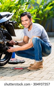 Asian Man Working On His Motor Scooter Looking At Camera