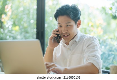 Asian man working while making phone call and using laptop at home