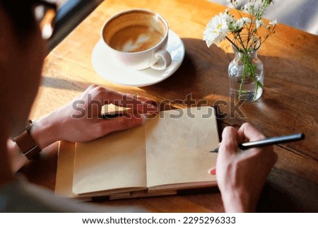 Asian man writing diary book journal with cup of coffee and flowers on wooden table 1