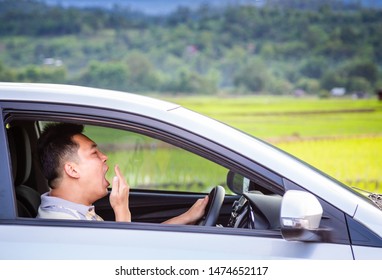 Asian man yawning in car,closeup tired,fatigued young man driving his car,male driver sleepy after long hours trip,green nature background,danger,accident,transportation and sleep deprivation concept