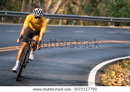 Asian man in yellow cycling jersey riding on road bike with willful face.
