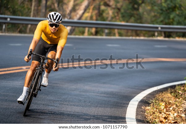 Asian man in yellow cycling jersey riding on road\
bike with willful face.