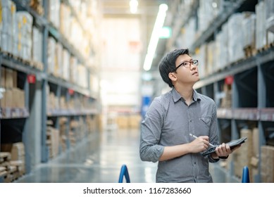 Asian manager man doing stocktaking of products in cardboard box on shelves in warehouse using digital tablet and pen. Male professional assistant checking stock in factory. Physical inventory count.