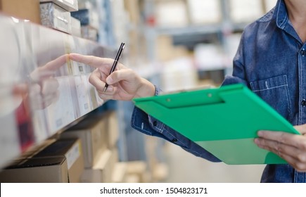 Asian manager man doing stocktaking of products management in cardboard box on shelves in warehouse using clipboard file and pen. Male professional assistant checking stock in factory. 