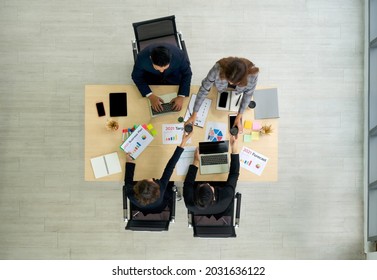 Asian Manager In A Suit And Team Examine The Documents On The Desk While The Secretary Brings The Coffee. Top View