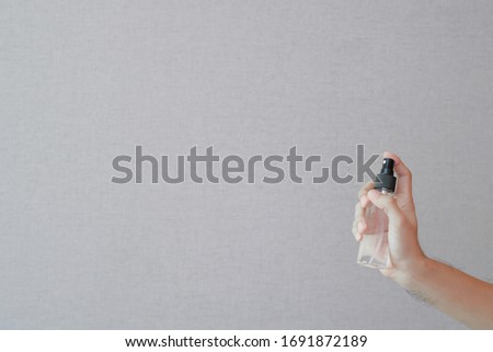 Asian man's hand holding alcohol or sanitizer spray bottle on grey wall background with copy space. Hygience and COVID-19 prevention concept.