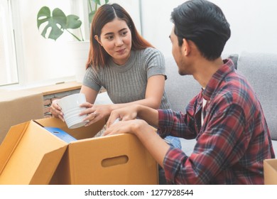 Asian Married Couple Start New Family Life Concept. Woman And Man Unpacking Messy Boxes After Moving In New House Together.