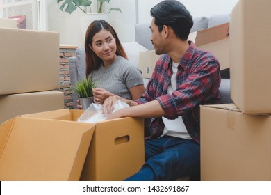 Asian Married Couple Start New Family Life Concept. Woman And Man Unpacking Messy Boxes After Moving In New House Together.