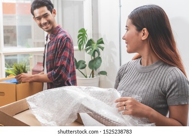 Asian Married Couple Start New Family Life Concept. Woman And Man Unpacking Messy Boxes After Moving In New House Together.