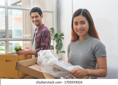 Asian Married Couple Start New Family Life Concept. Woman And Man Unpacking Messy Boxes After Moving In New House Together.