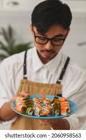 Asian master preparing sushi in restaurant. Man standing in the kitchen and sprinkles sesame seeds on sushi on the table. Healthy food nibble concept in restaurant. Fresh Food delivery concept