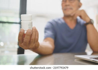 Asian Mature Adult Man Holding Medicine Bottle While Consulting With Doctor On Laptop From Home, Telehealth Or Telemedicine Concept