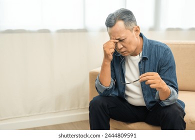 Asian mature old man sitting headache hands rubbing eye on sofa. Portrait of serious depressed senior asian man eye pain. Mature People and lifestyle - Powered by Shutterstock