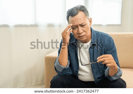 Asian mature old man sitting headache hands rubbing eye on sofa. Portrait of serious depressed senior asian man eye pain. Mature People and lifestyle