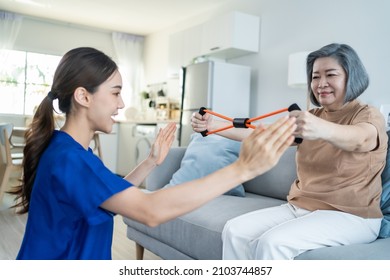 Asian mature older woman doing physiotherapist with support from nurse. Senior elderly female patient sitting on sofa in living room use resistance stretch band exercise with caregiver in nursing care