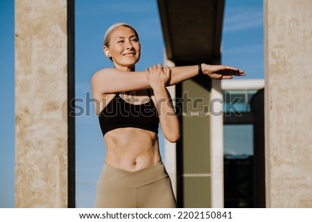 Asian mature woman in earphones doing exercise during workout outdoors