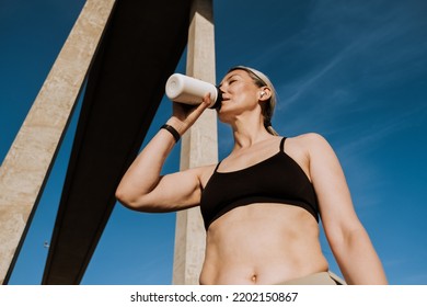 Asian Mature Woman In Earphones Drinking Water From Bottle During Workout Outdoors