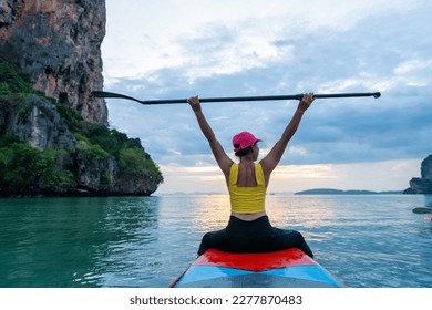 Asian mature woman sitting on paddle board and rowing in the ocean at tropical island at sunset. Wellness woman enjoy outdoor lifestyle and water sports surfing and paddle boarding on summer vacation. - Powered by Shutterstock