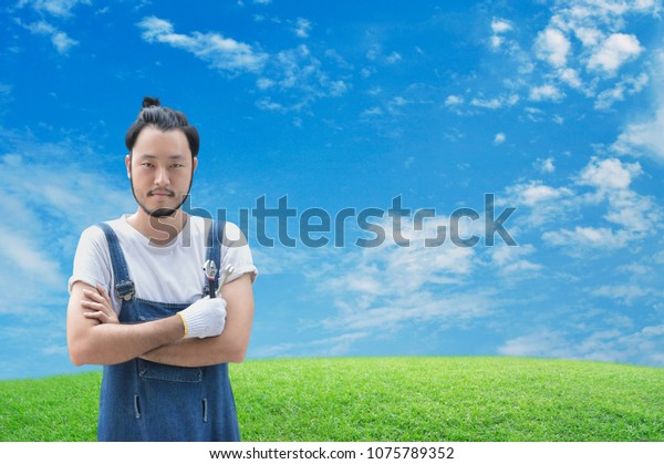 Asian mechanic car engine in uniform with tools\
over green grass field with blue sky, Business repair car on site\
service concept