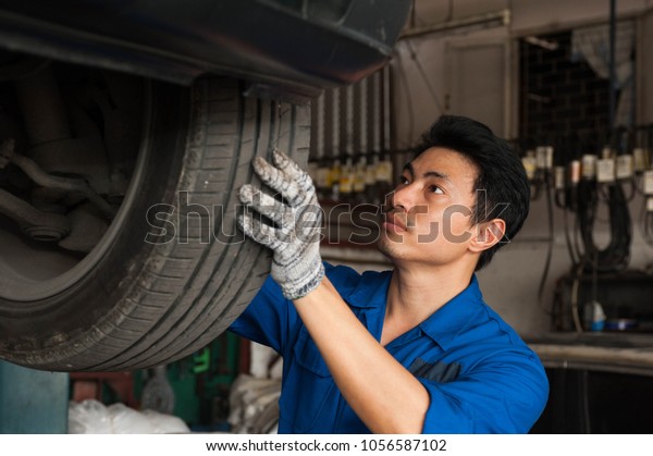 Asian mechanic is looking at the tire to check\
the condition