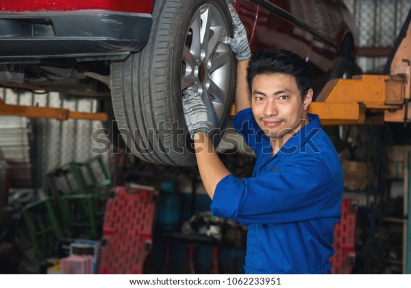 Asian mechanic looking under the car to\
repair the engine with work board in hand, japanese mechanic\
portrait style, mechanic maintenance working under\
car