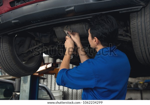 Asian mechanic looking under the car to\
repair the engine with work board in hand, japanese mechanic\
portrait style, mechanic maintenance working under\
car