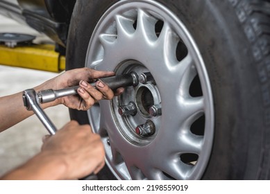 An Asian Mechanic Loosens And Removes The Lug Nuts From The Tire Of A Serviced Car With A Ratchet Lug Wrench. Removing A Wheel Manually. At An Auto Repair Shop.