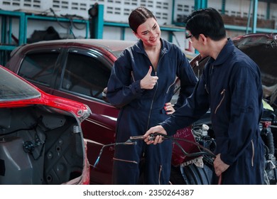 Asian mechanic man in uniform welding car body panel vehicle, beautiful woman technician coworker giving thump up, auto mechanic team fixing, repairing customer car automobile at garage repair service - Powered by Shutterstock